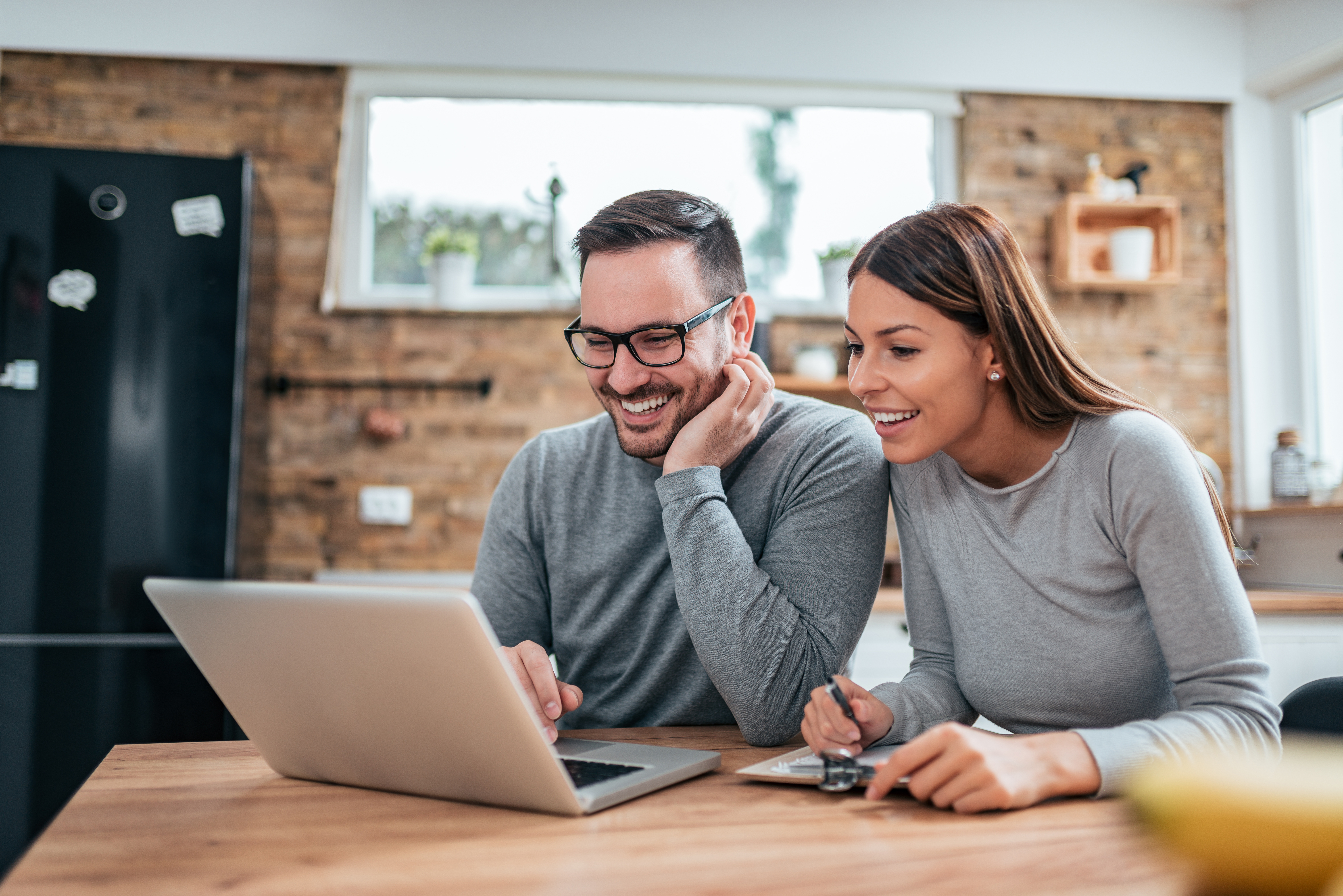 A young couple sits in their kitchen on a laptop.