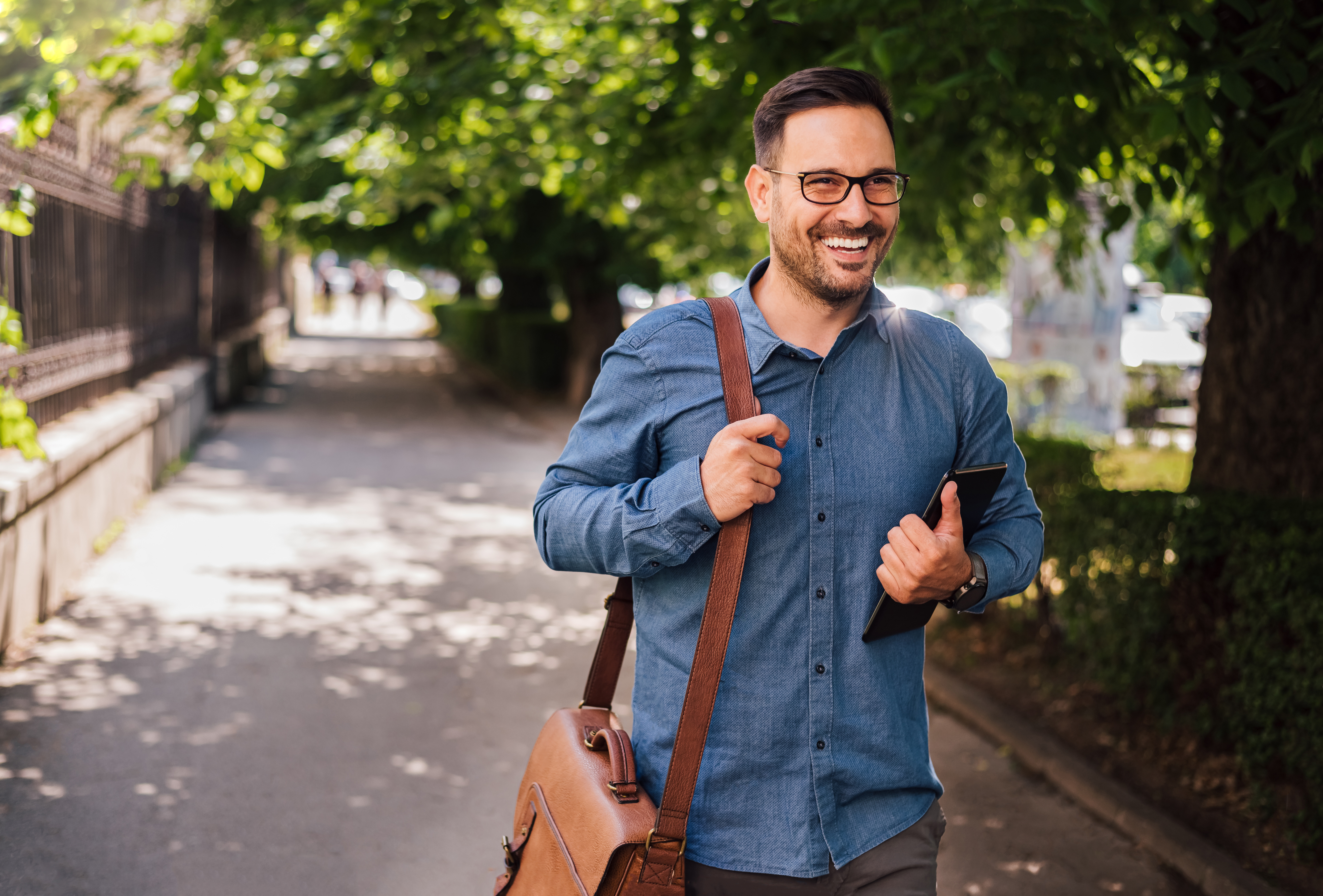 A man smiles in a city park on his way to work.